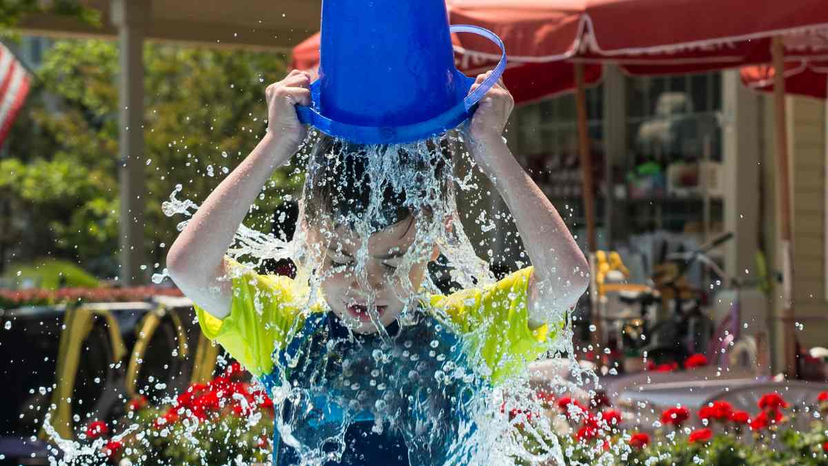 Niño echándose agua encima con un cubo azul para refrescarse e hidratarse en verano