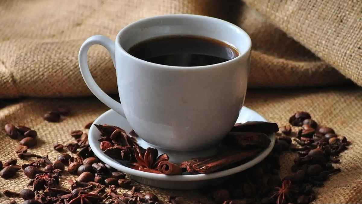 Taza de café negro sin azúcar sobre platillo con granos, forma sencilla que podría aumentar la esperanza de vida según la ciencia.