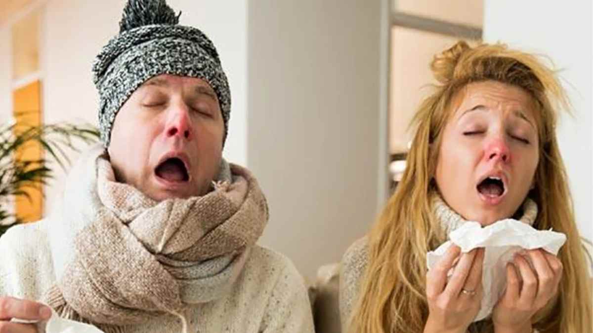 dos adultos con síntomas de gripe estornudando y usando pañuelos en un salón.