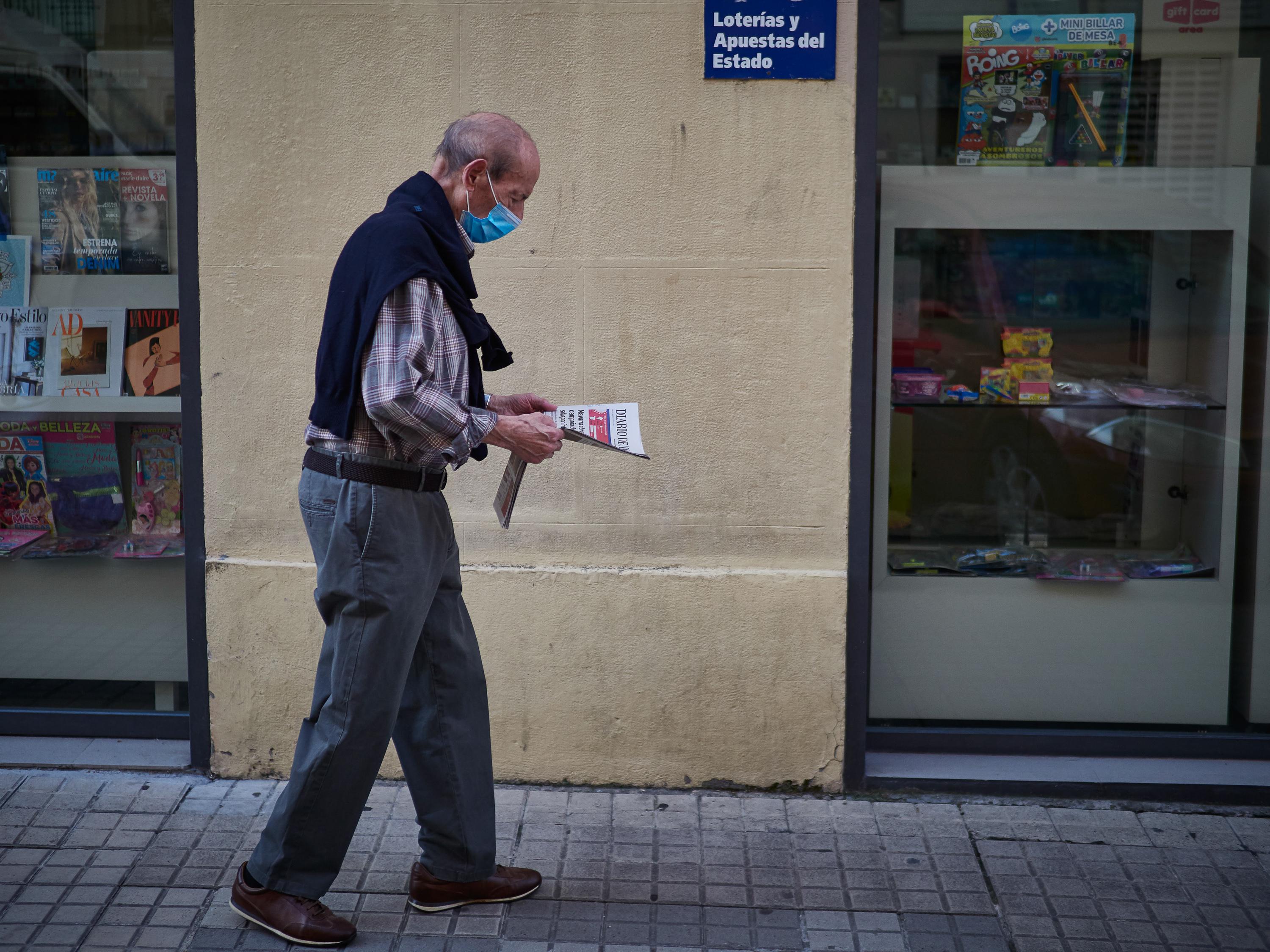 Un hombre camina con mascarilla leyendo un periódico / EP
