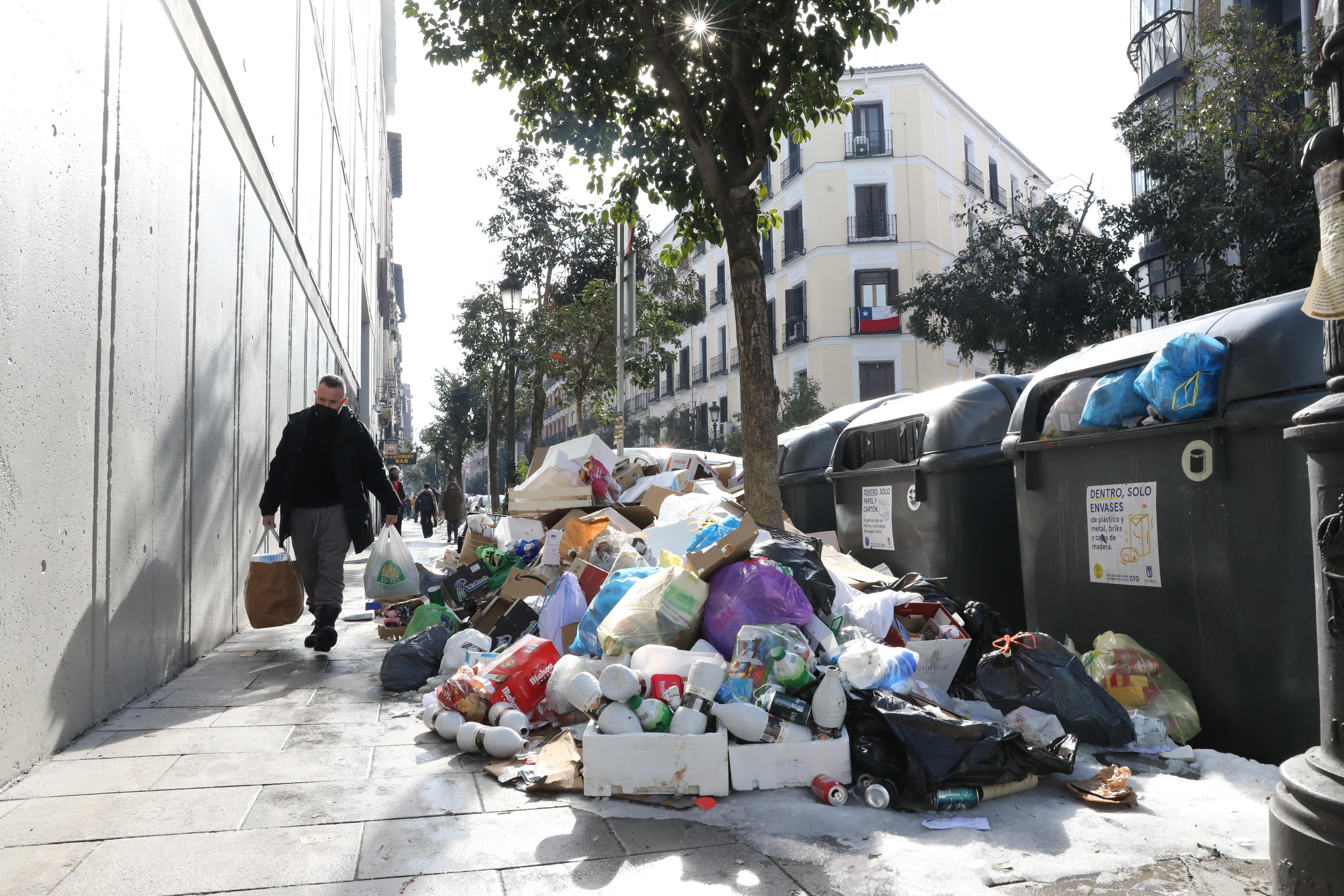 Transeúntes pasan al lado de decenas de bolsas de basura acumuladas en la calle Argumosa del barrio de Lavapiés de la capital, en Madrid (España), a 15 de enero de 2021
