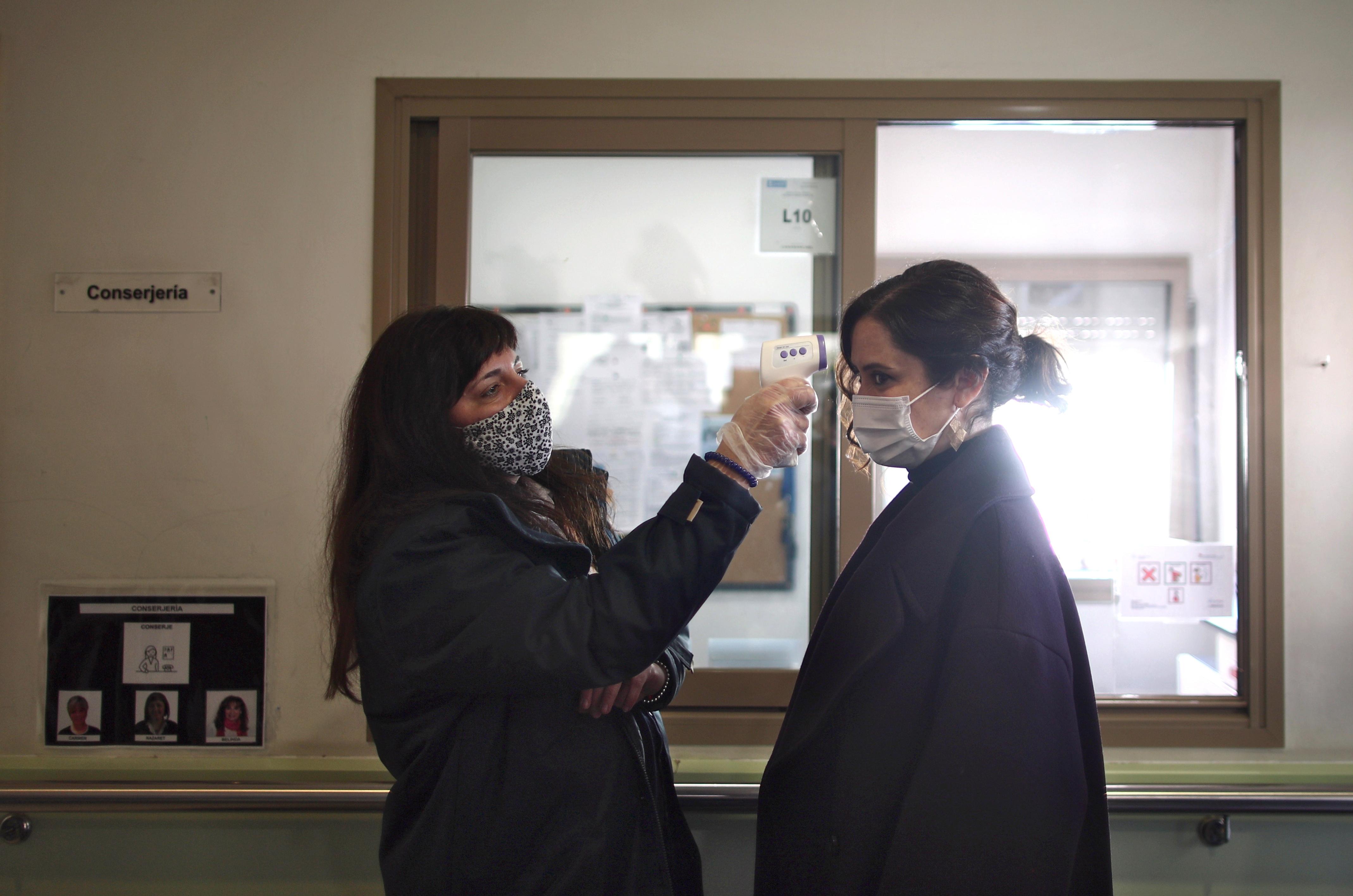 Una trabajadora le toma la temperatura a la presidenta de la Comunidad de Madrid, Isabel Díaz Ayuso