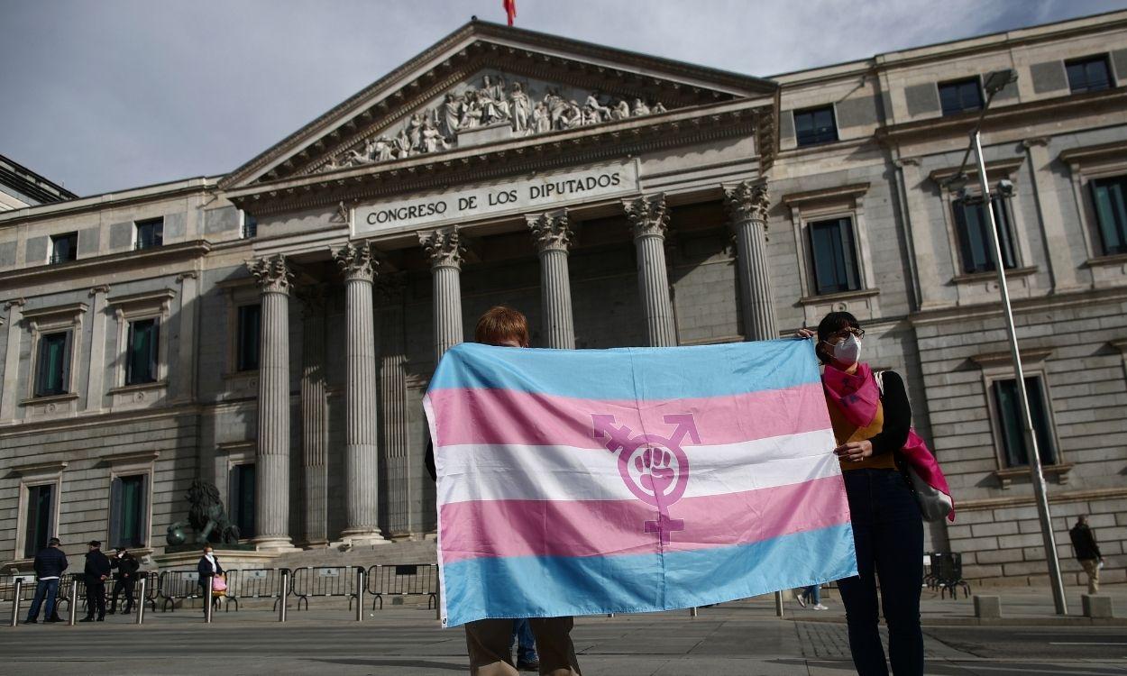 Dos personas sostienen una bandera trans durante una concentración convocada frente al Congreso de los Diputados en Madrid. Europa Press.
