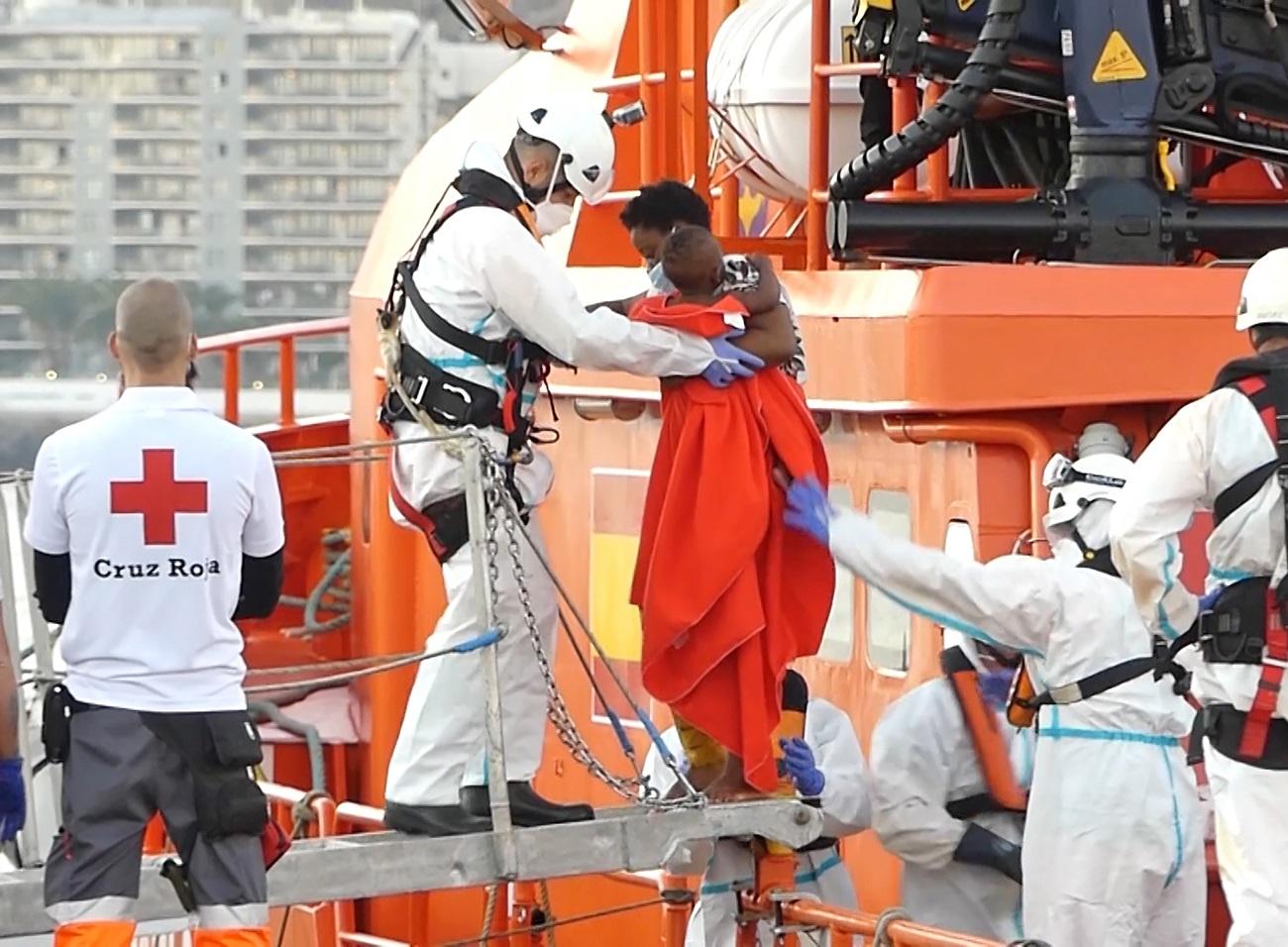 Un miembro de la Cruz Roja ayuda a bajar del barco a una mujer migrante con su niño en el puerto de Arguineguín (Gran Canaria, España) a 17 de marzo de 2021. Fuente: Europa Press.
