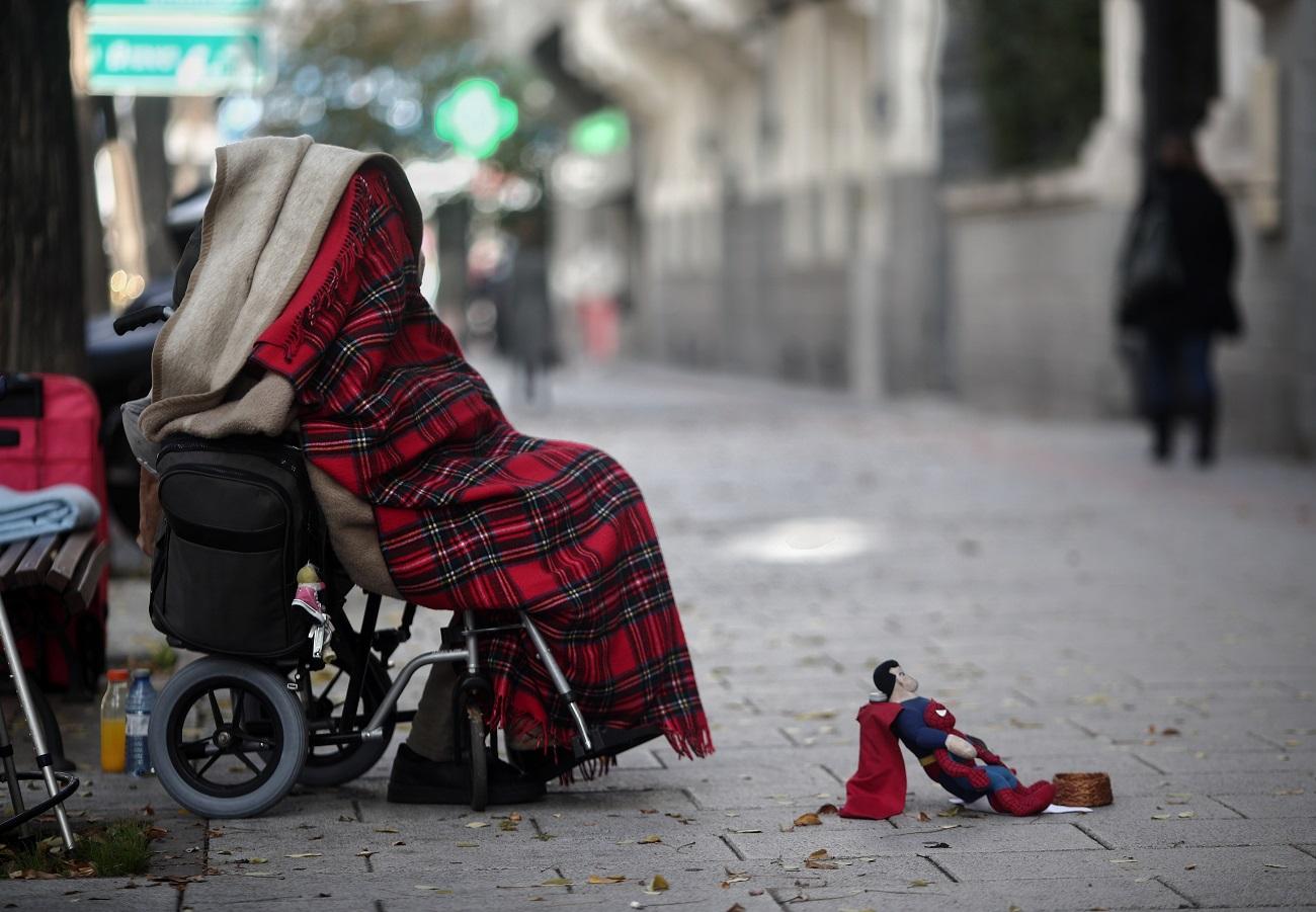Una persona en silla de ruedas y tapada con una manta pide dinero con un muñeco de Superman en una céntrica calle durante la segunda ola de la pandemia del coronavirus, en Madrid. Fuente: Europa Press.
