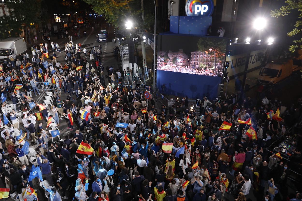 Seguidores del Partido Popular celebran con banderas de España los primeros sondeos en las inmediaciones de la sede del partido durante la jornada electoral
