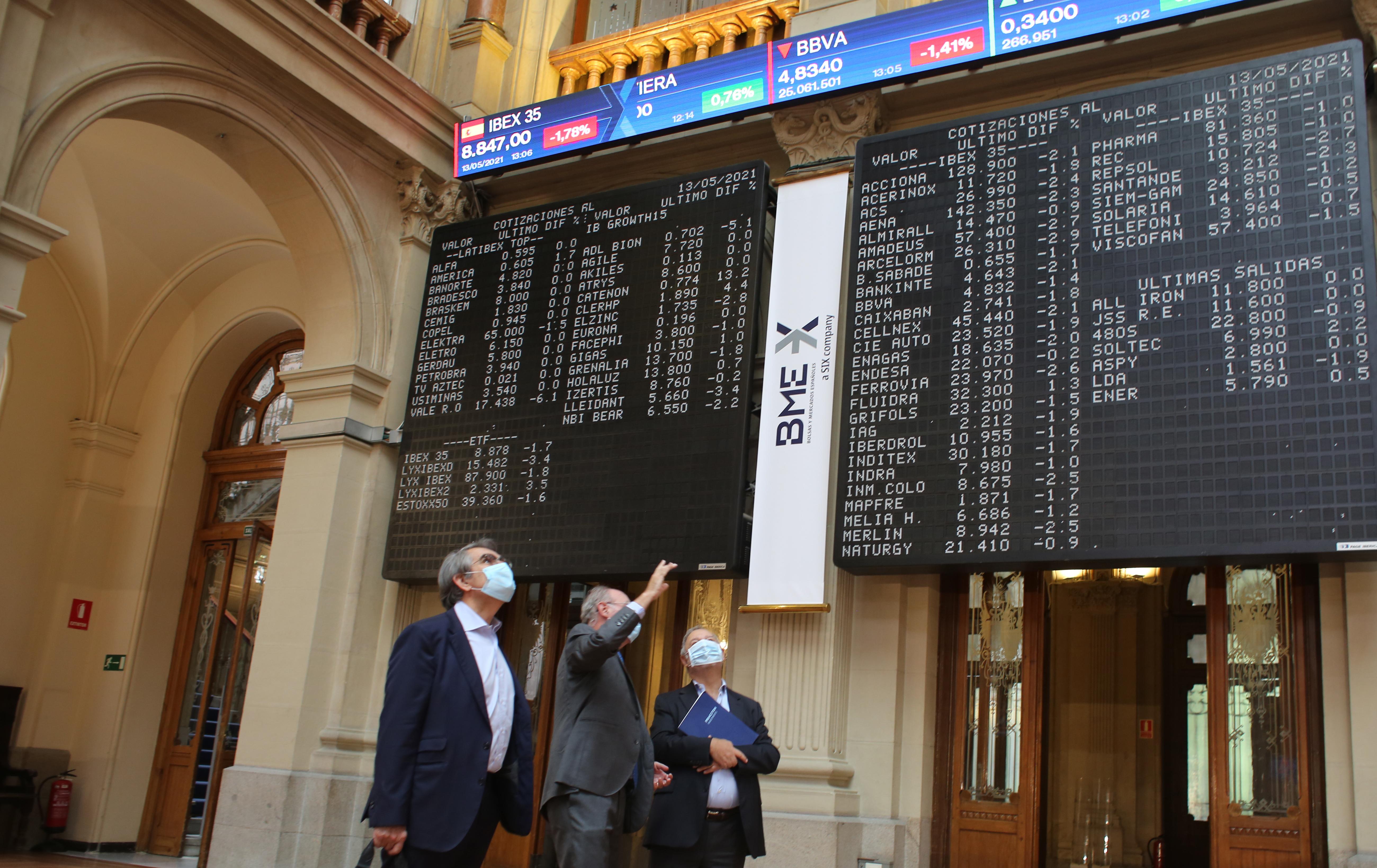 Tres hombres observan valores económicos en el Palacio de la Bolsa en Madrid (España).