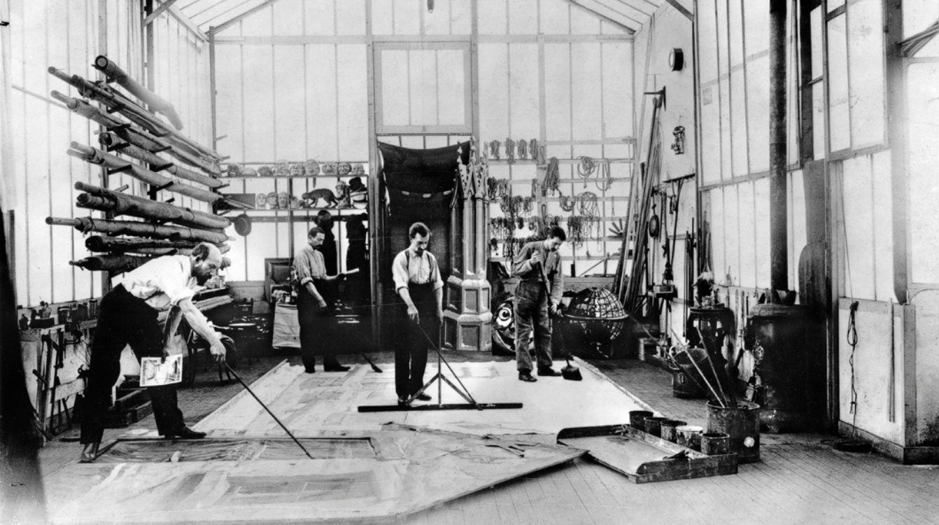 Georges Méliès pintando un decorado en el suelo de su estudio, con dibujo preparatorio en una de las manos