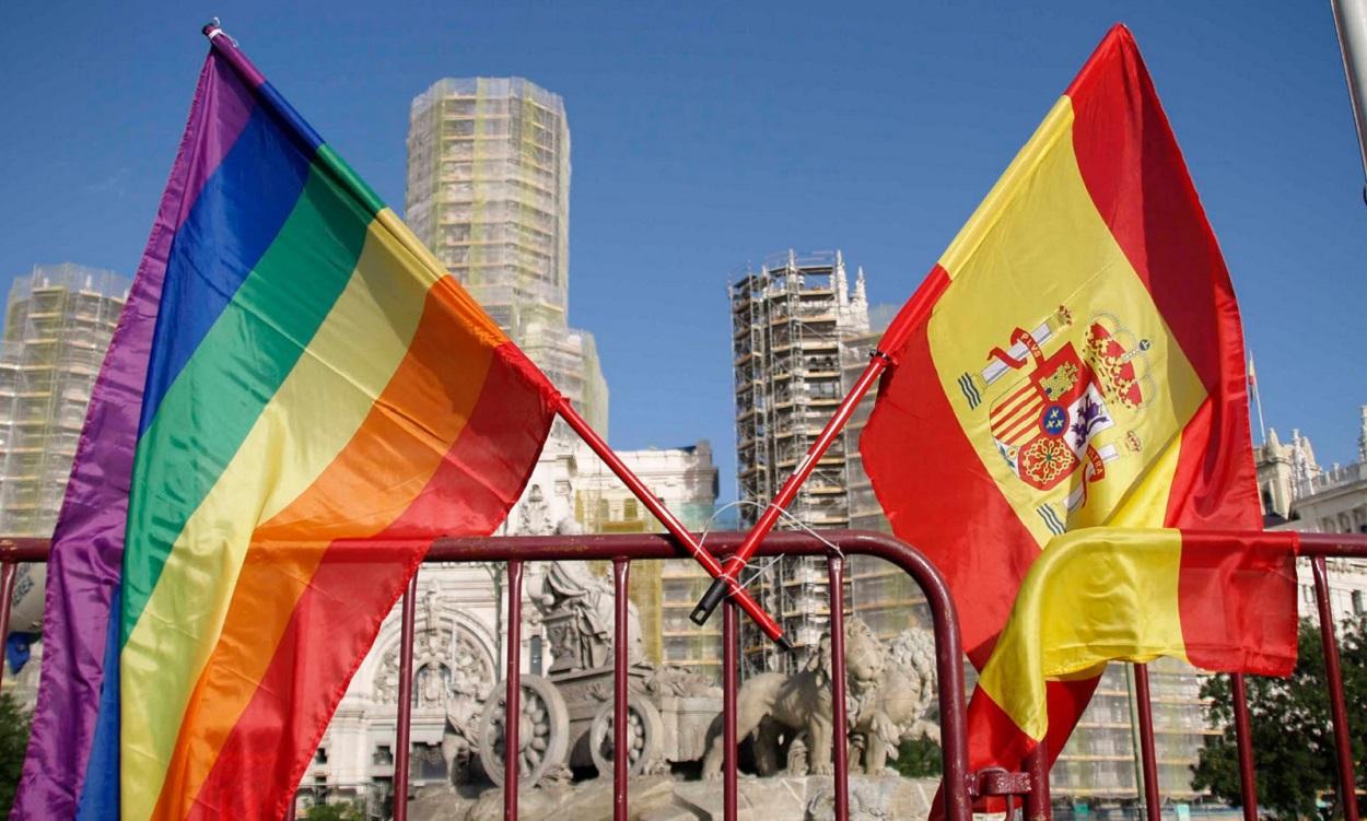 Una bandera arcoiris junto a una bandera de España