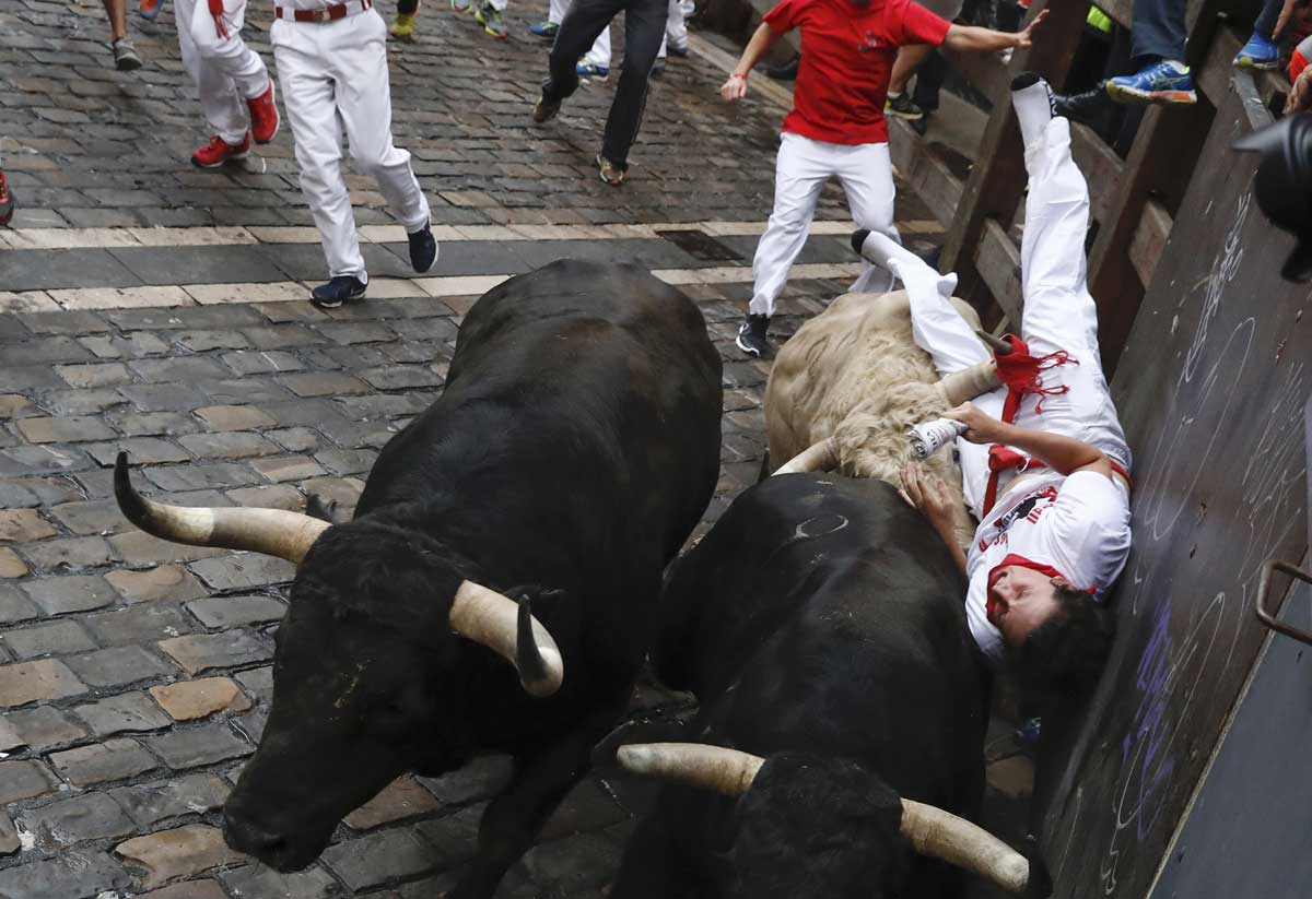 Los toros de la ganadería de Jandilla, de Mérida (Badajoz), atrapan a un mozo contra la barrera en la curva de Mercaderes durante el quinto encierro de los Sanfermines 2017. 