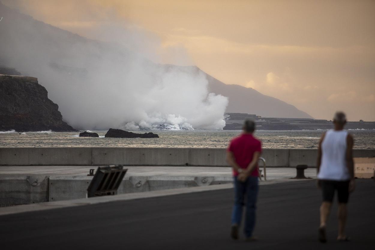Dos personas observan la columna de humo y la lava del volcán de Cumbre Vieja a su llegada al Océano Atlántico. Kike Rincón / Europa Press