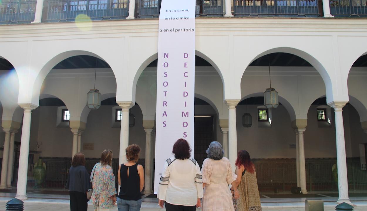 Diputadas de Adelante Andalucía ante la pancarta desplegada en un patio del Parlamento.