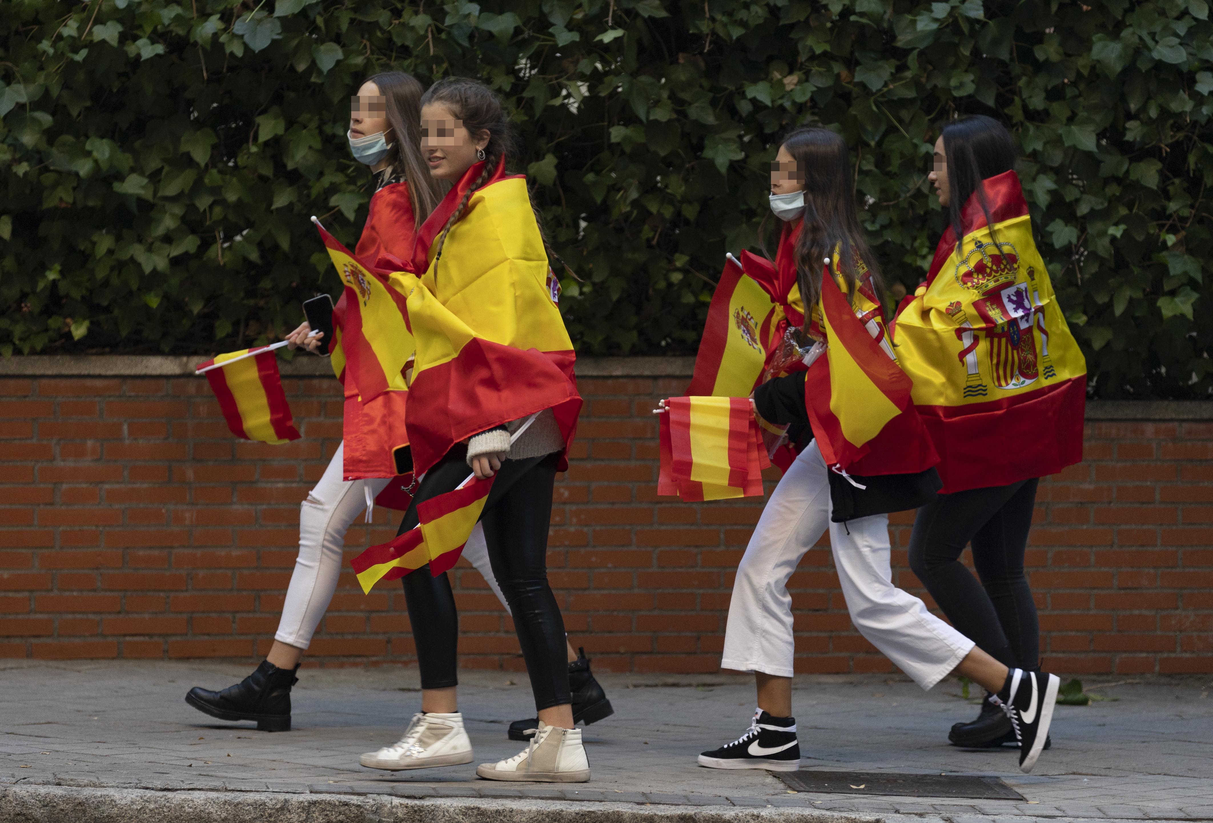 Cuatro jóvenes tapadas con la bandera de España se dirigen al acto solemne de homenaje a la bandera nacional y desfile militar en el Día de la Hispanidad.