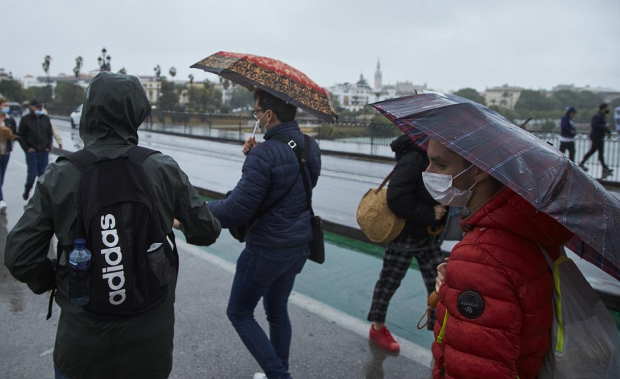 Un grupo de personas cruzando el Puente de Isabel II en un día lluvioso en Sevilla. EP
