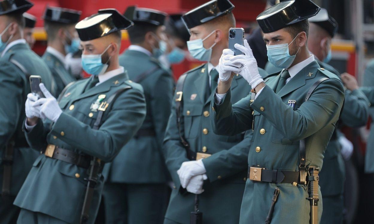 Agentes de la Guardia Civil miran sus móviles antes de que comience el acto solemne de homenaje a la bandera nacional y desfile militar en el Día de la Hispanidad