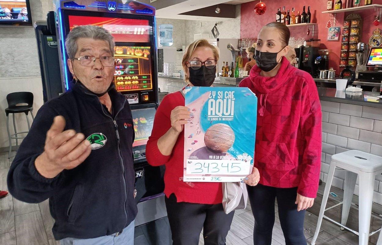 Remedios y Esmeralda posan con el cartel junto a uno de los clientes agraciados en su bar de Almería. EP