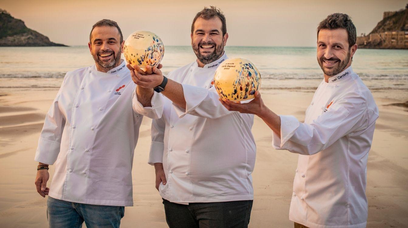 Los cocineros premiados con Tres Soles Repsol,  'Iván Cerdeño' (Toledo) y los hermanos Padrón de 'El Rincón de Juan Carlos', en Tenerife, posan con su escultura conmemorativa en la playa de San Sebastián