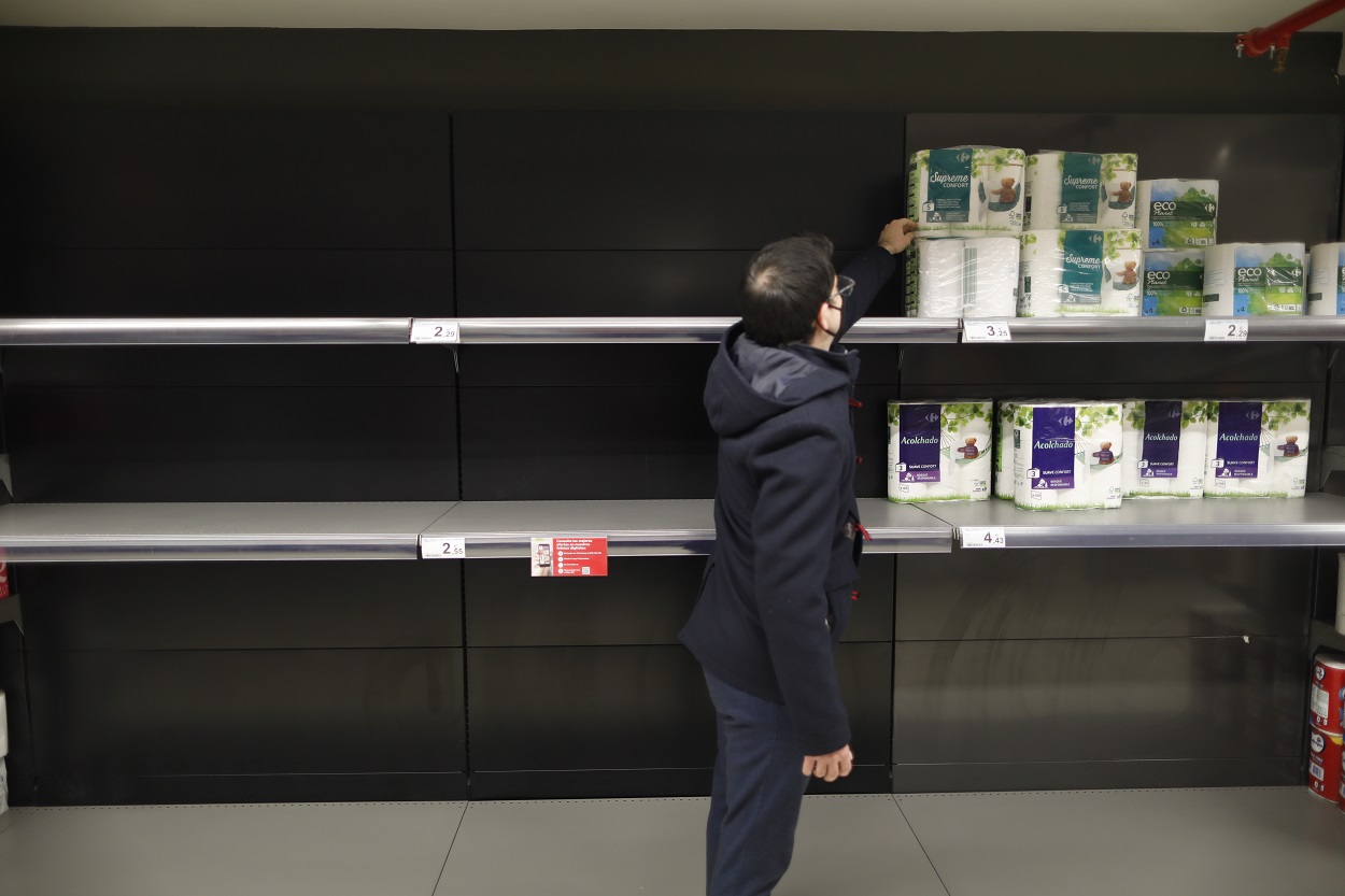 Un hombre coge papel higiénico de su estantería a la que le faltan productos. Fuente: Europa Press.