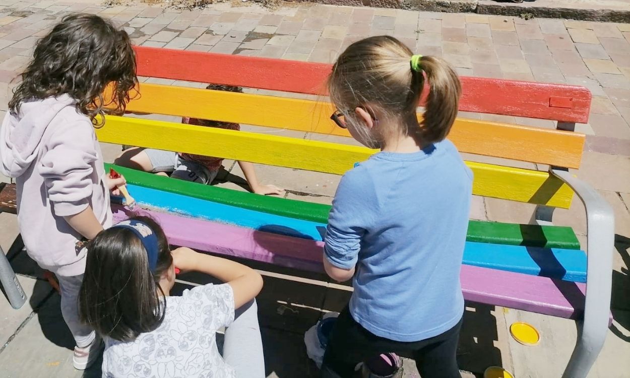 Niñas pintando con los colores de la bandera LGTBI+ un banco que fue vandalizado con los de la bandera de España