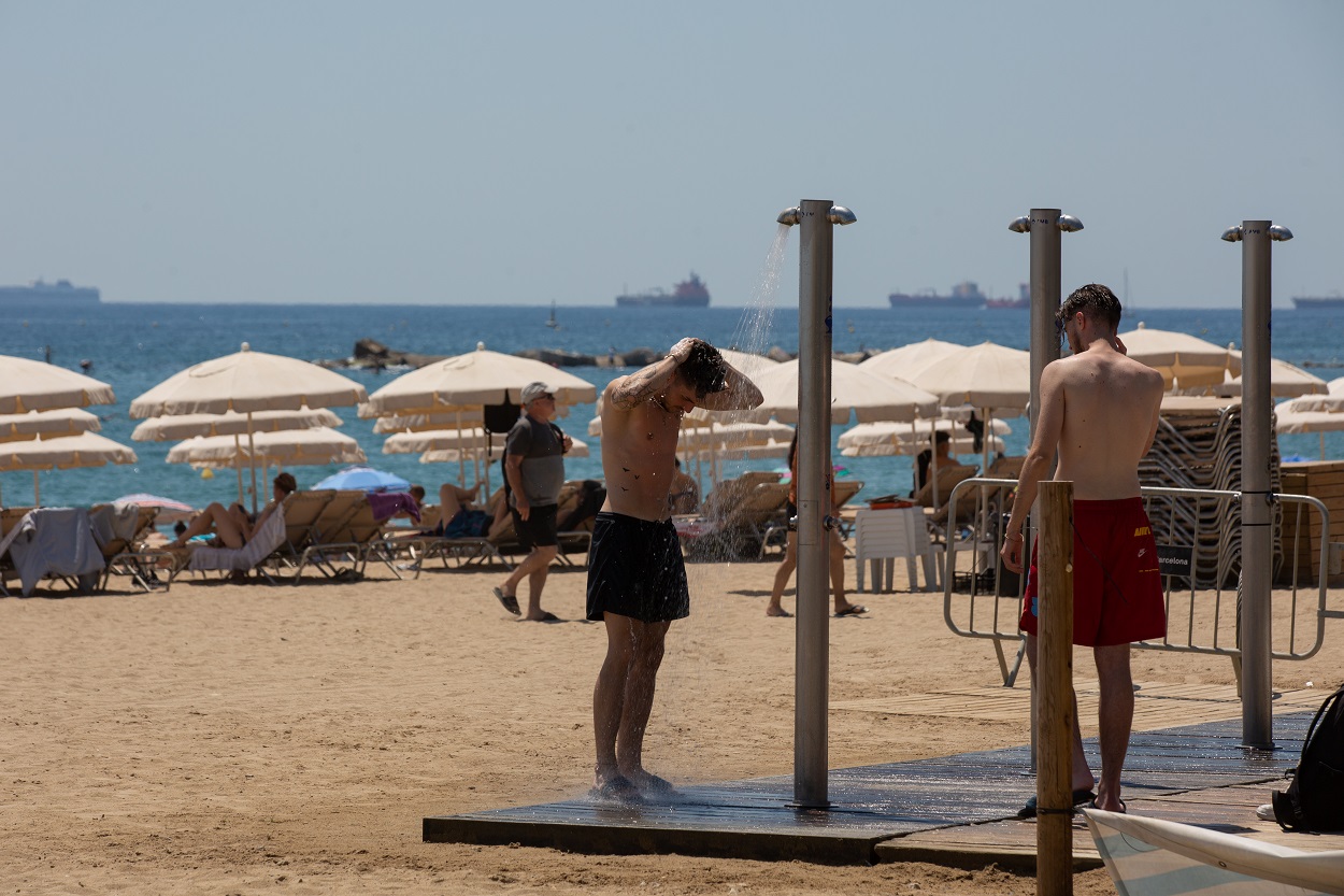 Varias personas refrescándose en las duchas de la playa de la Barceloneta. EP / David Zorrakino