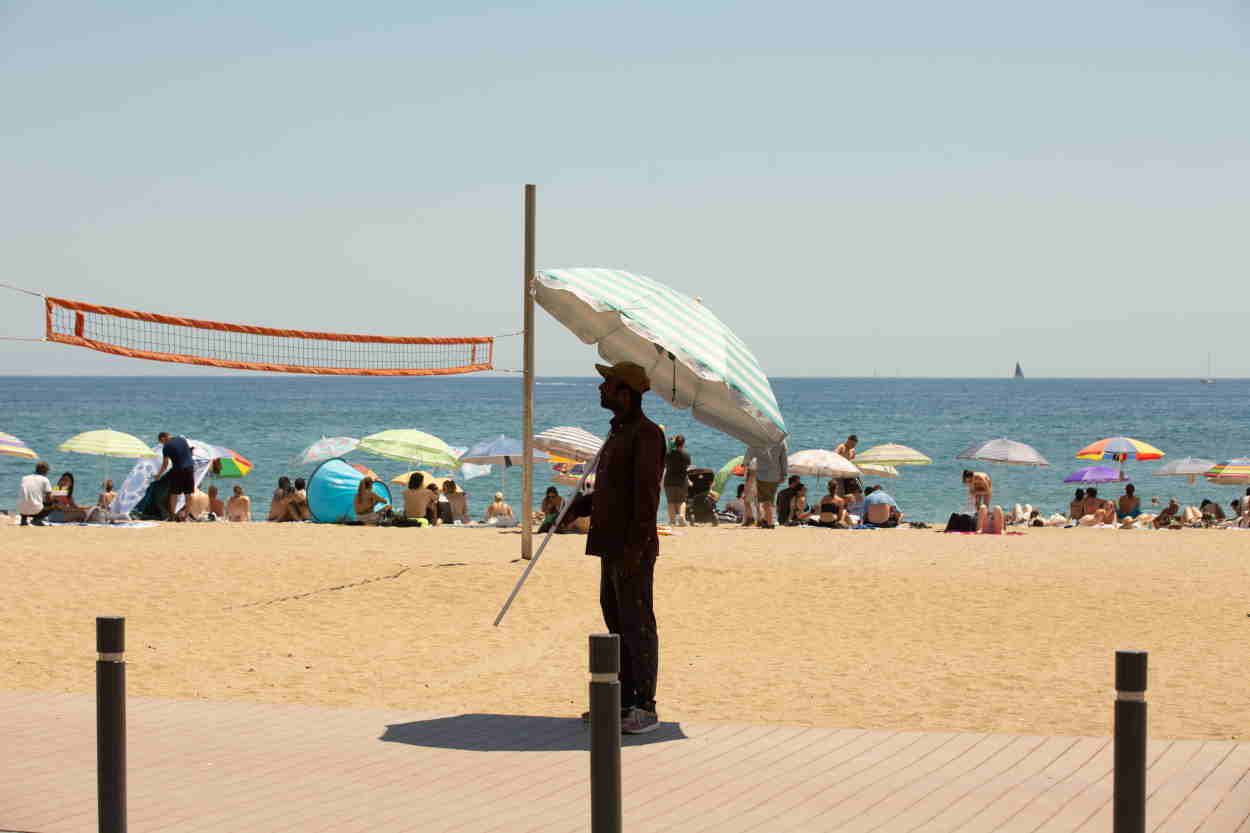 Un hombre se tapa con una sombrilla en la playa de la Barceloneta (Barcelona). E.P