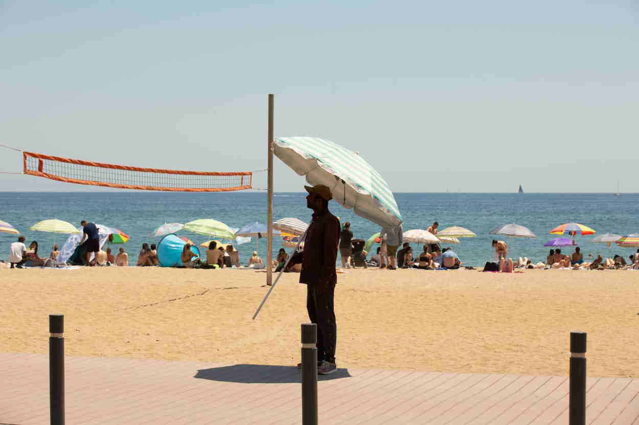 Un hombre se tapa con una sombrilla en la playa de la Barceloneta (Barcelona). EP