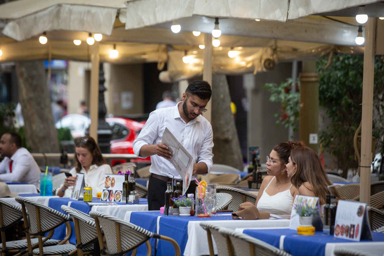 Un camarero atiende a dos clientas en la terraza. EP