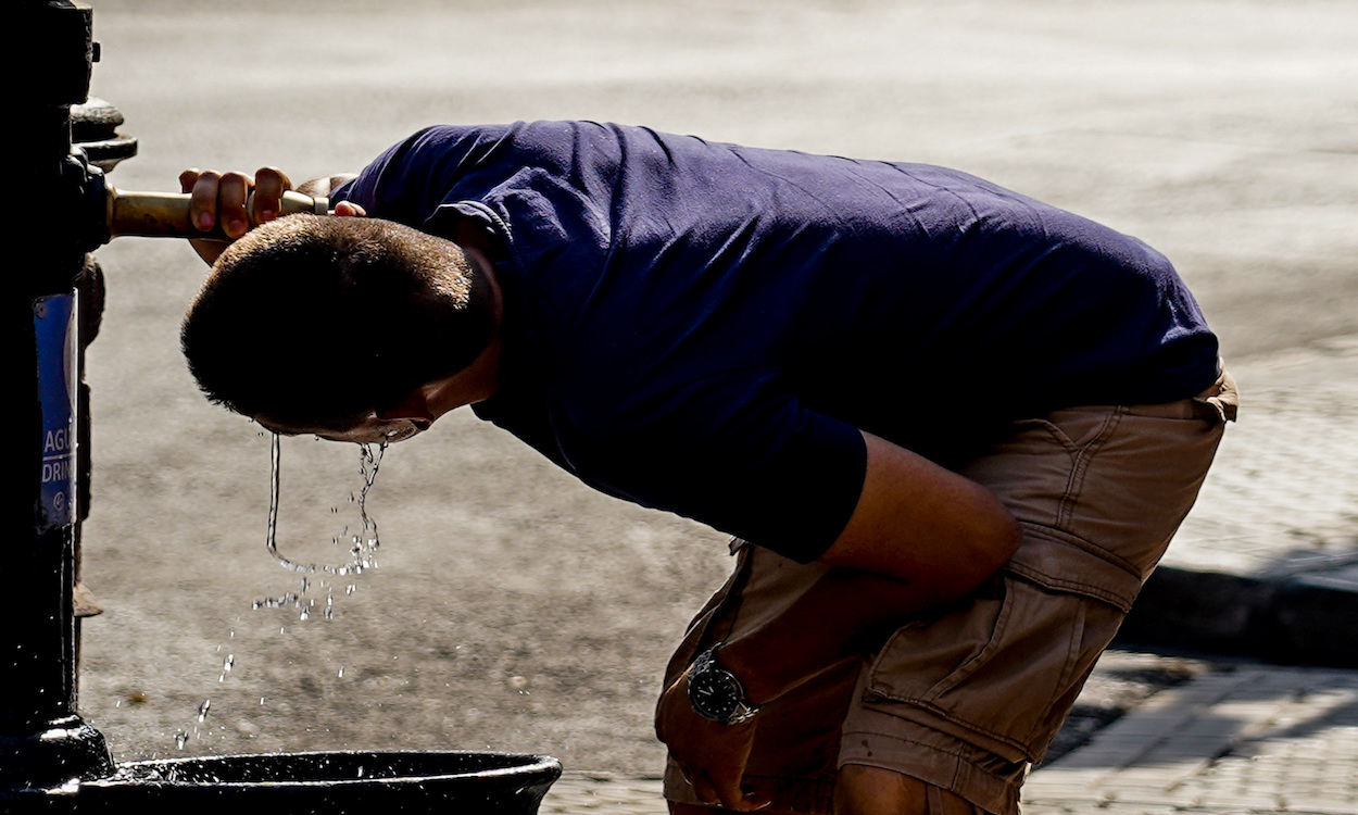 Un joven bebe agua en una fuente en un día con altas temperaturas. EP