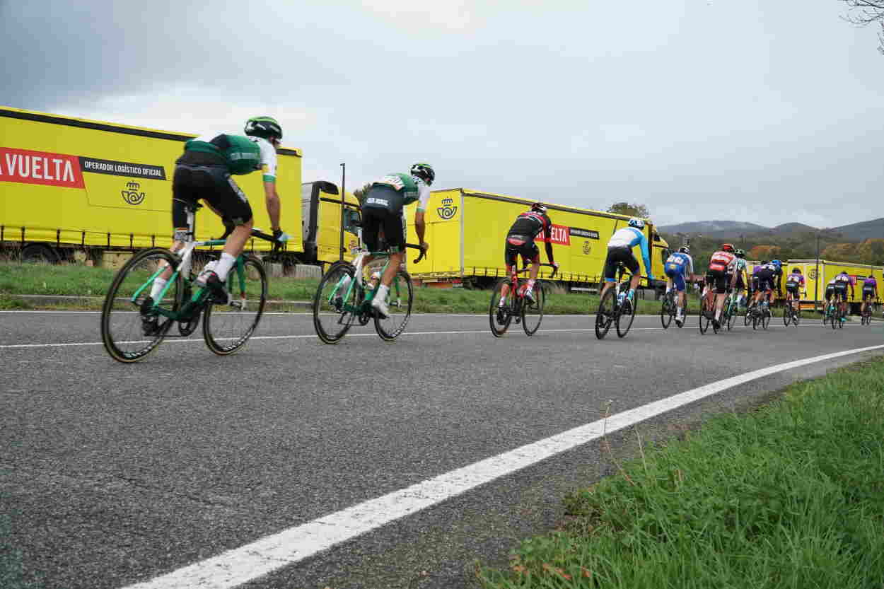 Imagen de corredores de La Vuelta junto a camiones de Correos