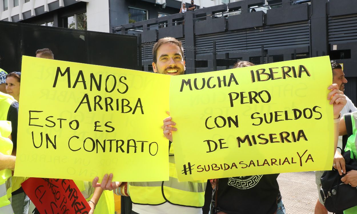 Dos personas sostienen pancartas en una concentración de tripulantes de cabina (TCP) de Iberia, en Trabajadores de Iberia con carteles durante una concentración, frente a las oficinas centrales de la compañía, a 26 de