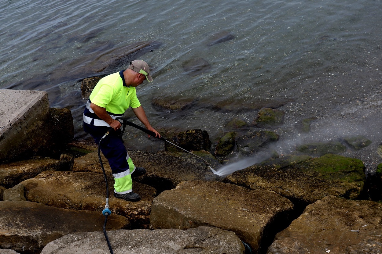 Un operario limpia las rocas manchadas en la playa de Poniente de La Línea con el vertido del OS35. EP.