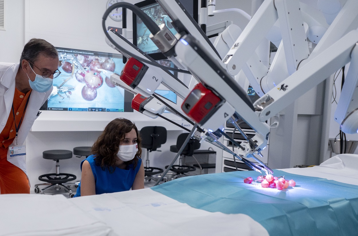 La presidenta de la Comunidad de Madrid, Isabel Díaz Ayuso, observa como el robot Da Vinci manipula uvas de muestra en una de las salas del nuevo Centro Quirúrgico del Hospital público Gregorio Marañón. EP.