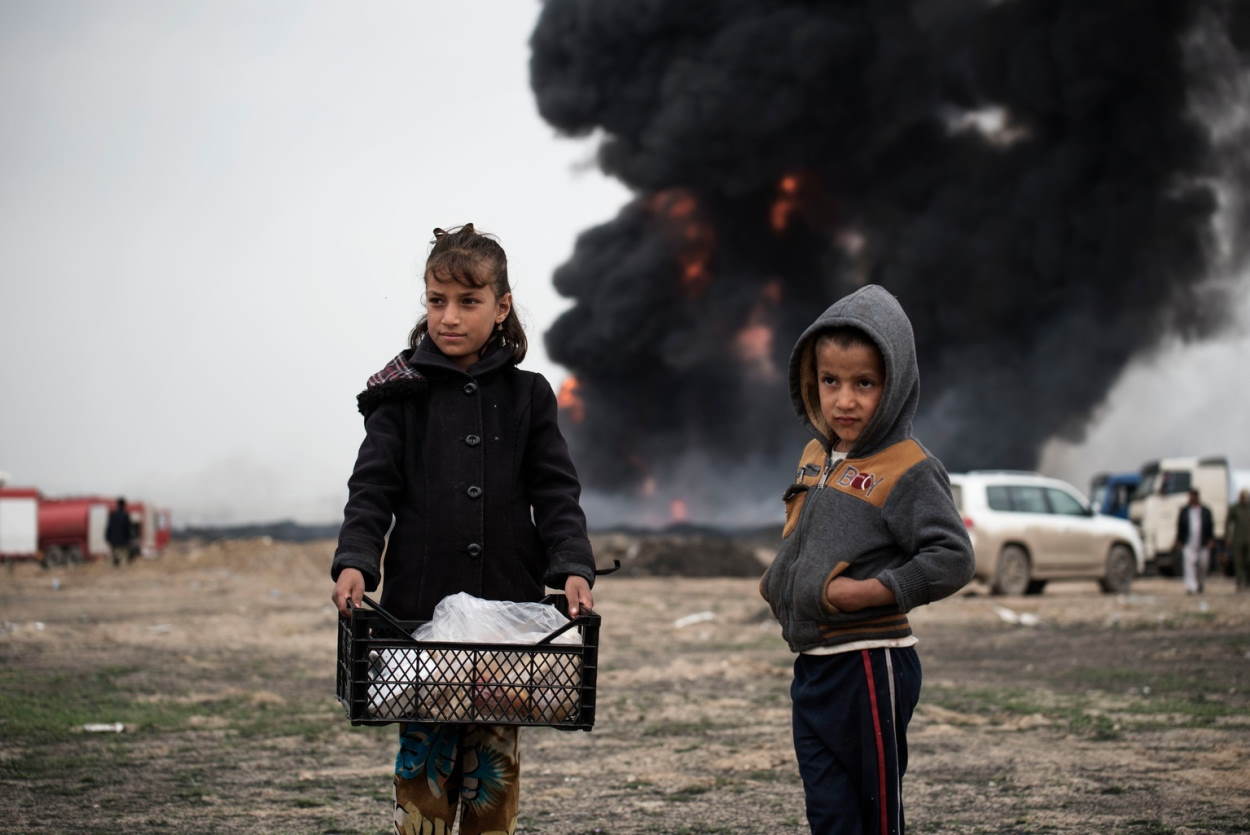 Niños llevan comida a los bomberos mientras intentan extinguir los pozos de petróleo incendiados por los miembros de ISIS. EP