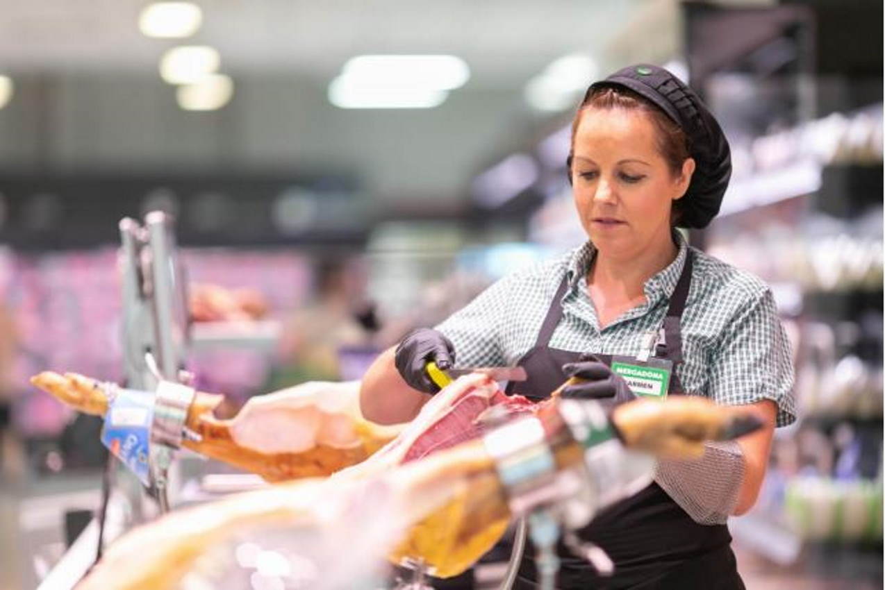 Empleada de Mercadona corta a cuchillo una pata de jamón.