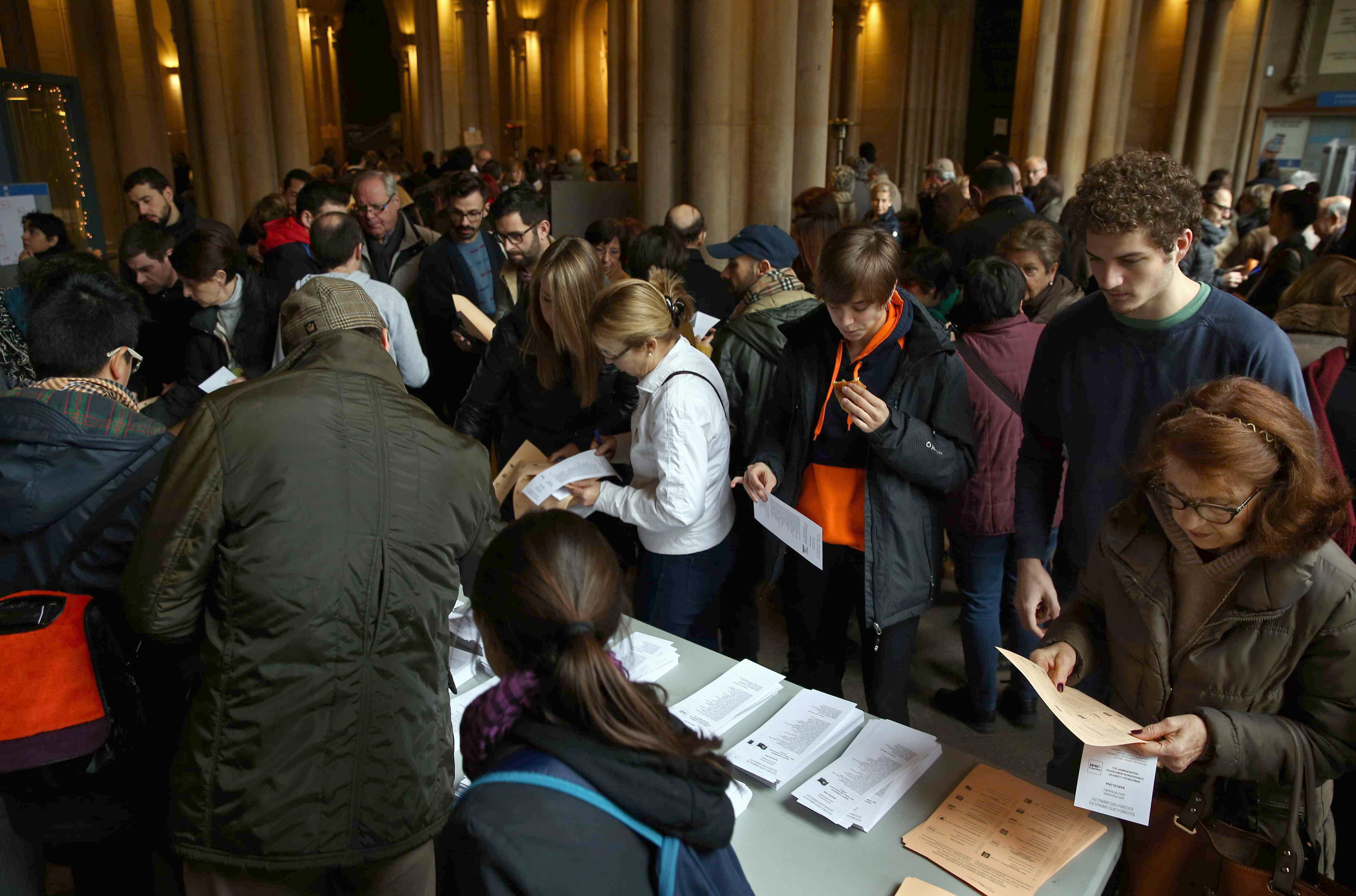 Los ciudadanos escogen las papeletas para ejercer su voto en las elecciones generales, antes de incorporarse a la cola en el colegio electoral situado en la Universitat de Barcelona. EFE/Toni Albir