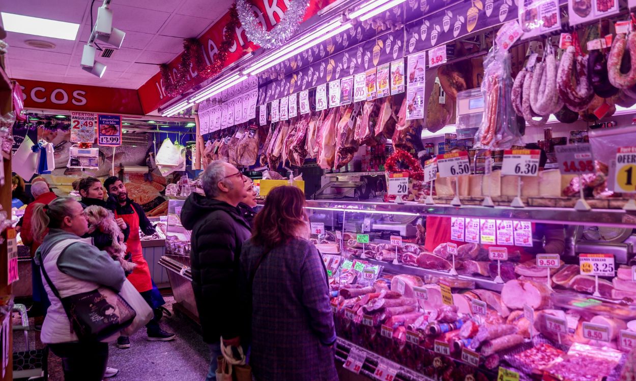Varias personas esperan su turno en la charcutería para realizar sus últimas compras en la tienda de comestibles ‘Los Mares Alimentación’, en el barrio de Prosperidad