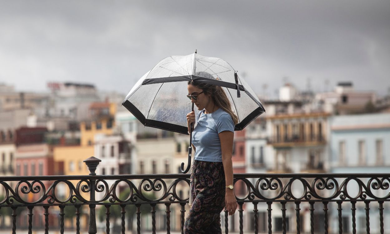 Una mujer camina por la calle en verano bajo el cielo nublado y la lluvia en España. EP