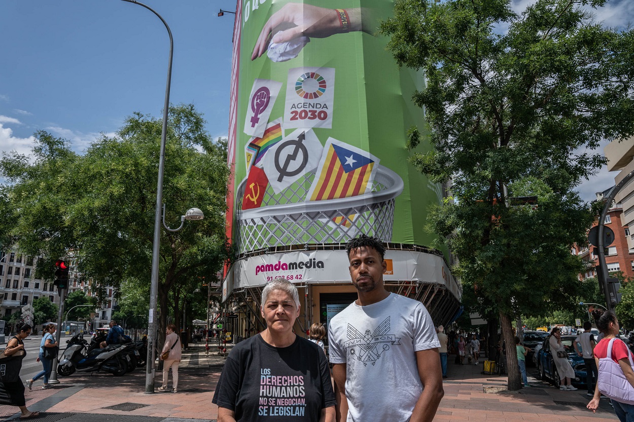 La presidenta de la Federación Estatal LGTBI+, Uge Sangil y el presidente de COGAM, Ronny de la Cruz, posan frente a la lona que Vox ha instalado en la calle Alcalá, 145. EP.