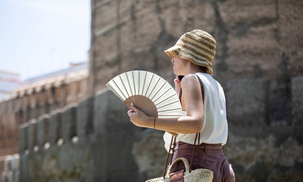 Una mujer se protege del sol con sombrero y abanico en Sevilla. EP
