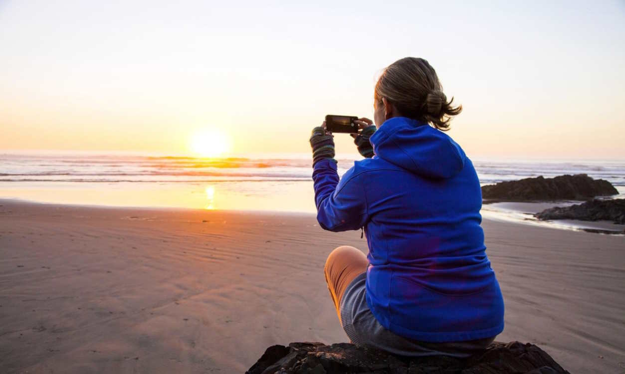 Una joven captura el atardecer en la playa con su smartphone