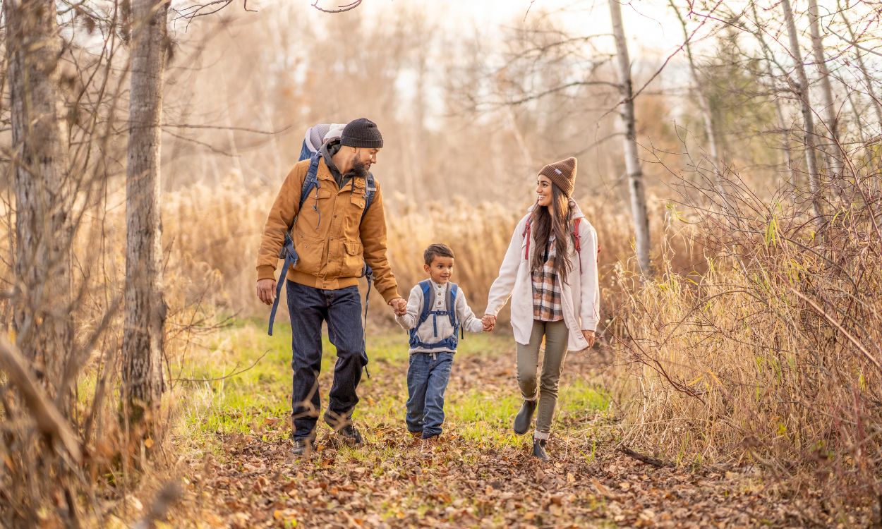 Dos padres y un niño haciendo una ruta de senderismo en otoño. Canva