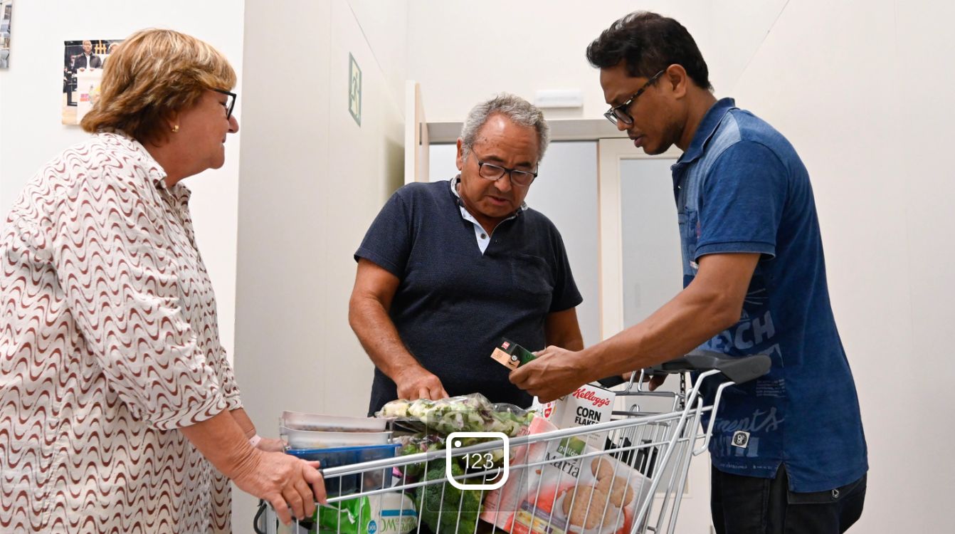 Montse y Ramón, voluntarios de la entidad social De Veí a Veí, entregan un lote a un usuario del banco de alimentos.