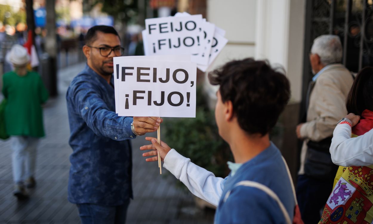 Dos personas sujetan pancartas que aluden a Alberto Núñez Feijóo en el acto del PP en Madrid. EP.