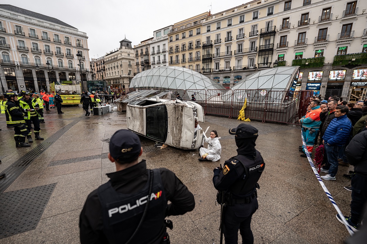 Dos agentes de Policía Nacional delante de una activista de Greepeace con un vehículo, tras realizar una acción en la Puerta del Sol. Diego Radamés / Europa Press