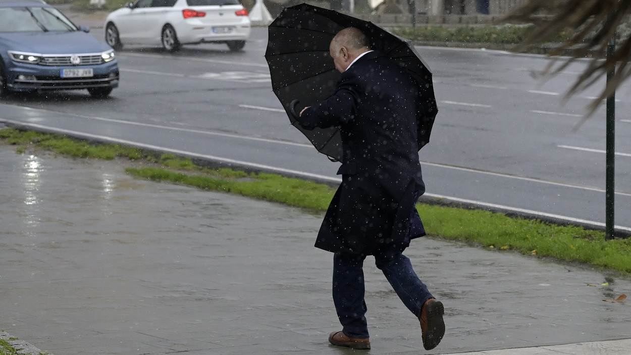 Un hombre con paraguas trata de refugiarse del viento y de la lluvia en Galicia. EP