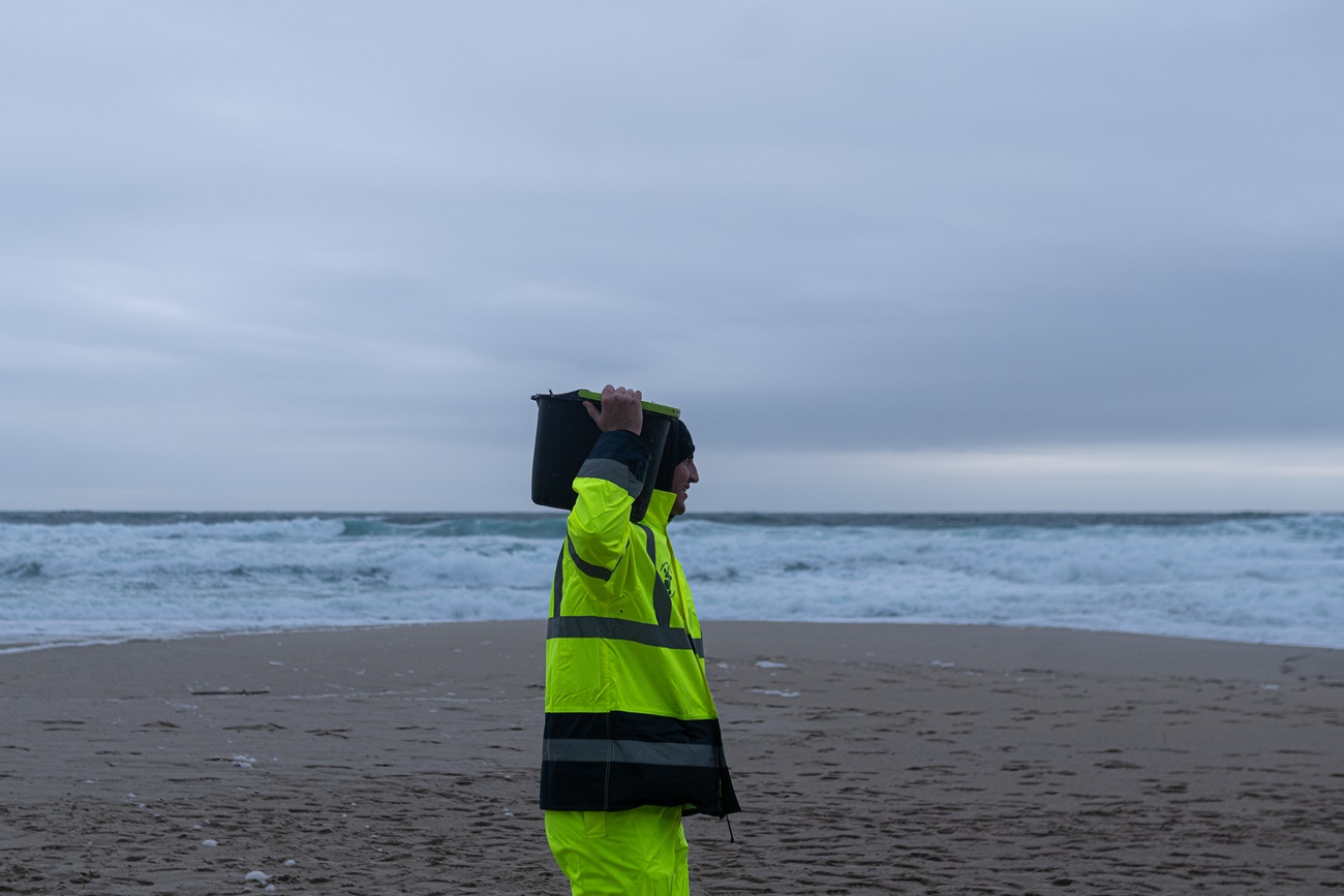 Un hombre carga un cubo con pélets en la playa del Dique, en Queiruga (A Coruña)