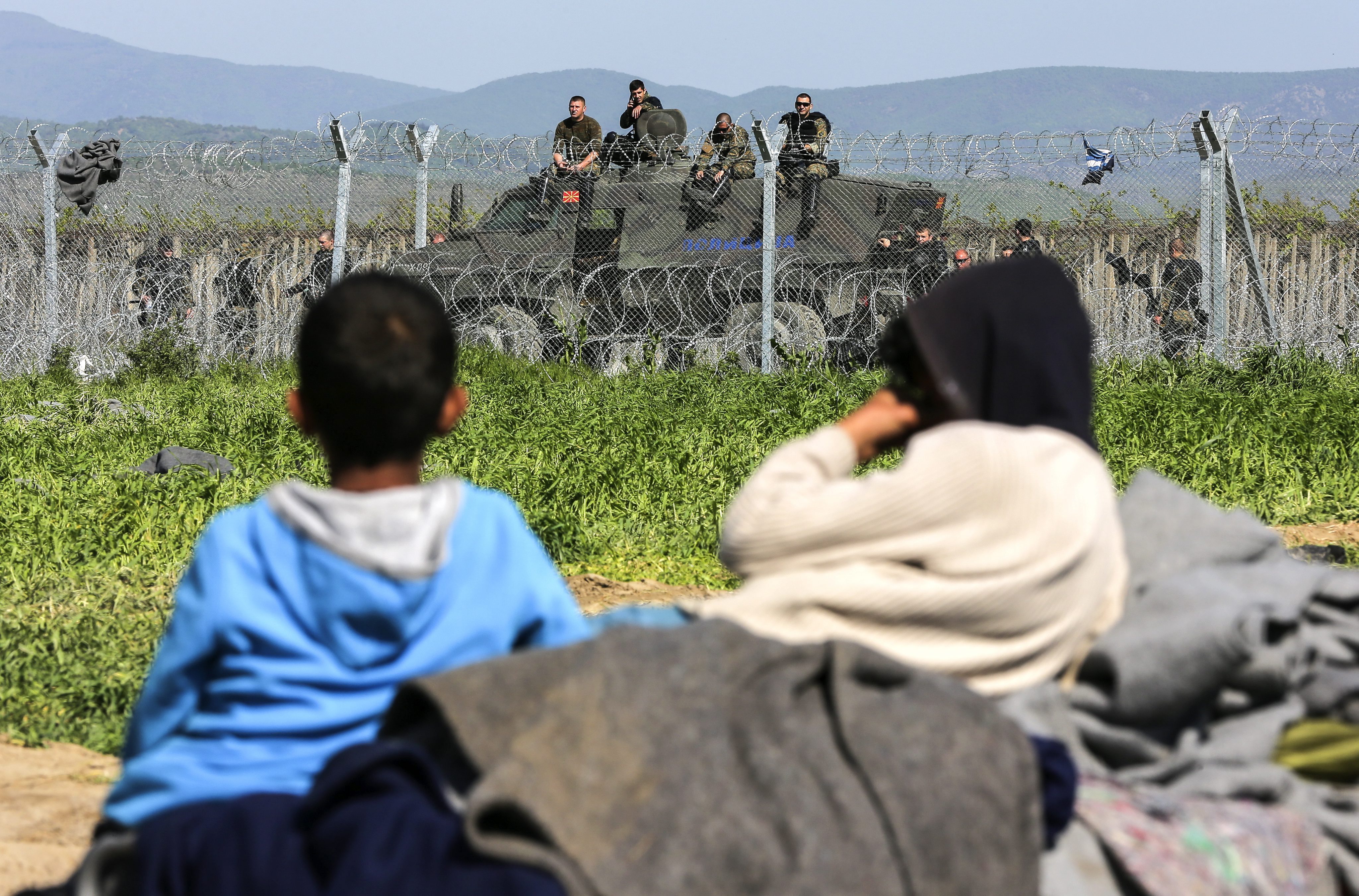 Unos niños descansaban el martes junto a la valla fronteriza del campamento de refugiados de Idomeni, en Grecia, mientras la policía macedonia hacia guardia al otro lado.