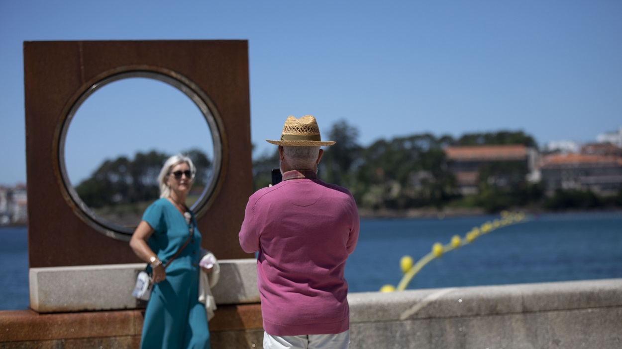 Un hombre echa una foto a una mujer en el paseo marítimo de la playa de Sanxenxo. EP