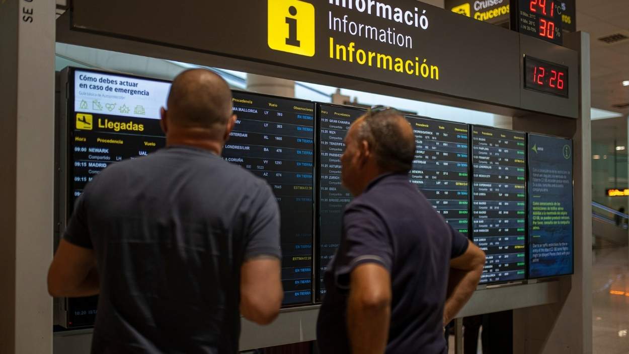 Varias personas observan un panel de llegadas en el aeropuerto de Barcelona. EP.