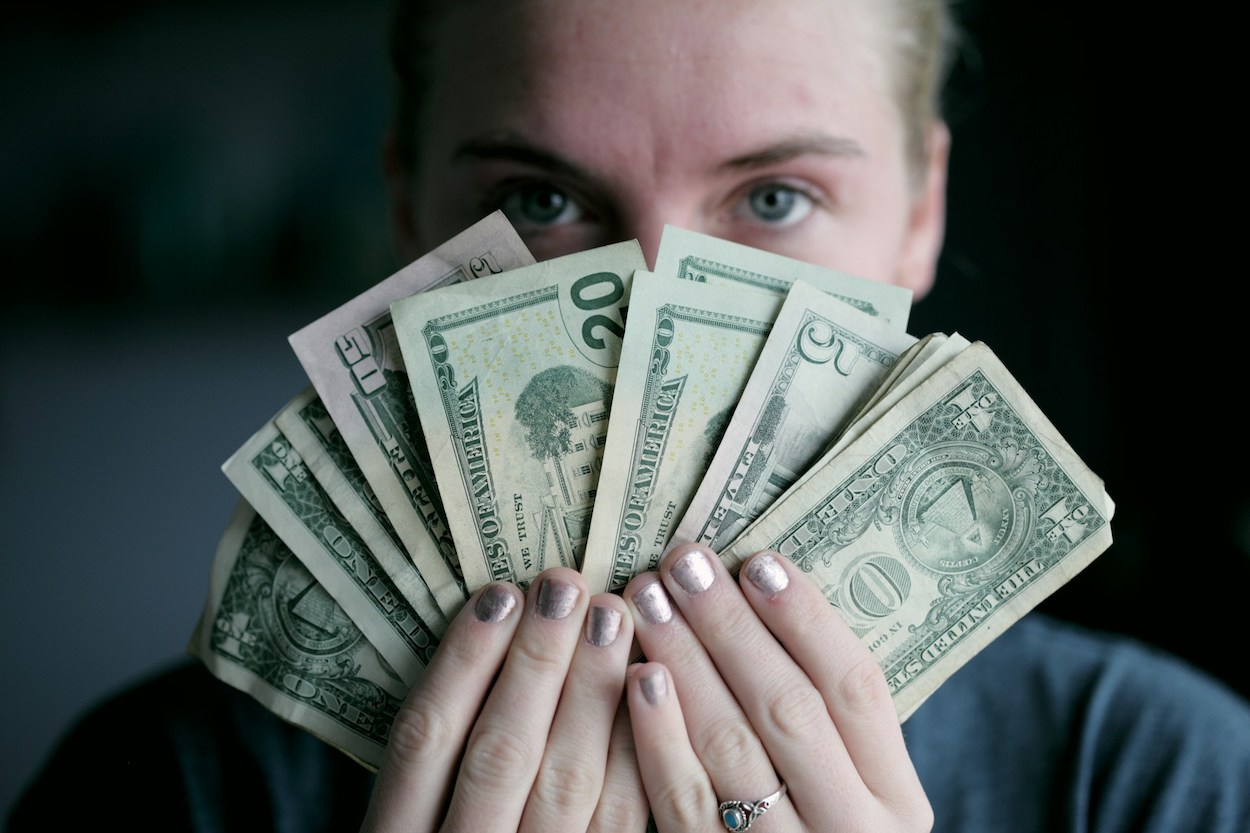 Mujer joven sostiene un abanico de billetes / Foto de Alexander Grey / UNSPLASH